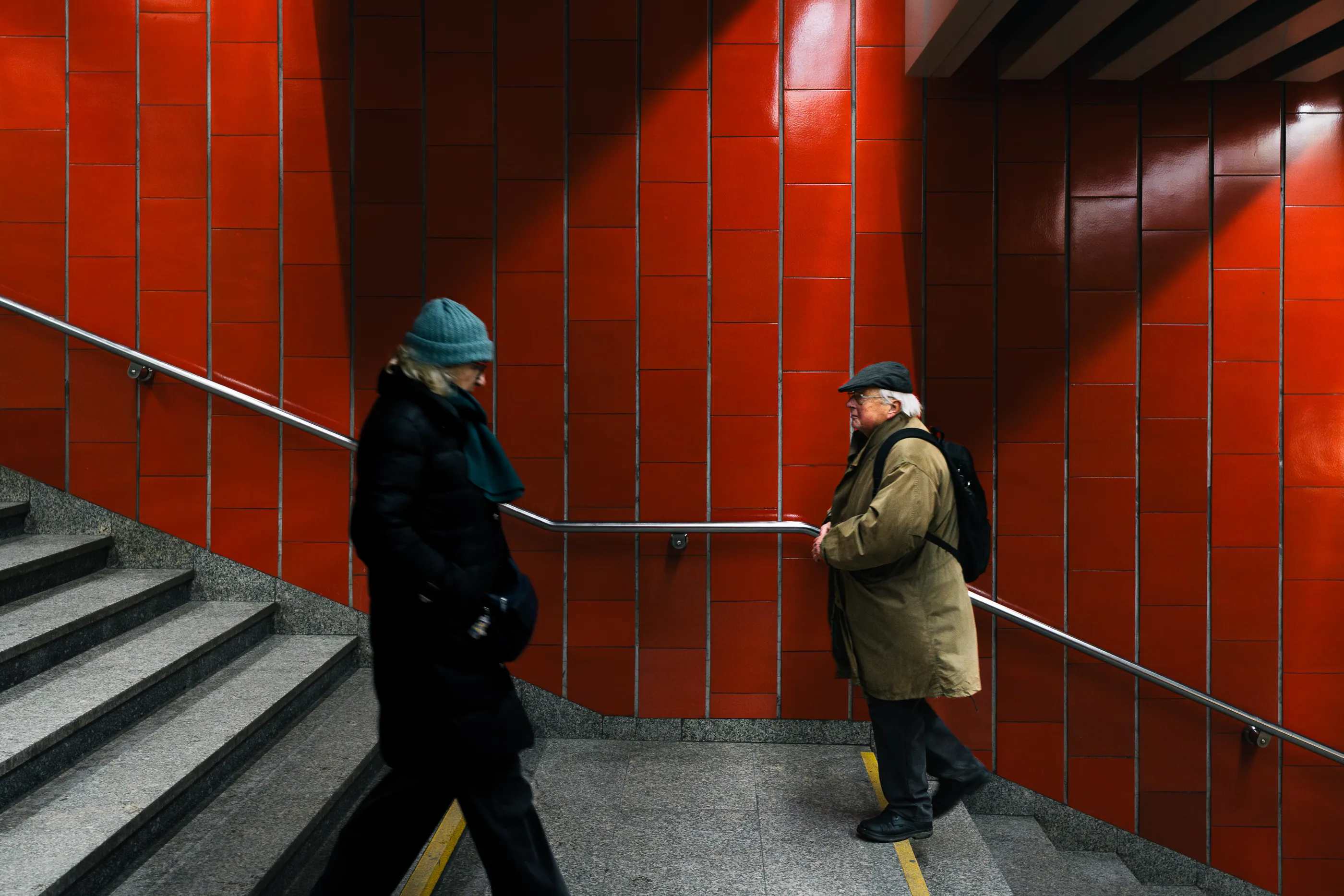 Two commuters cross paths on a staircase inside a red-tiled Warsaw underpass.