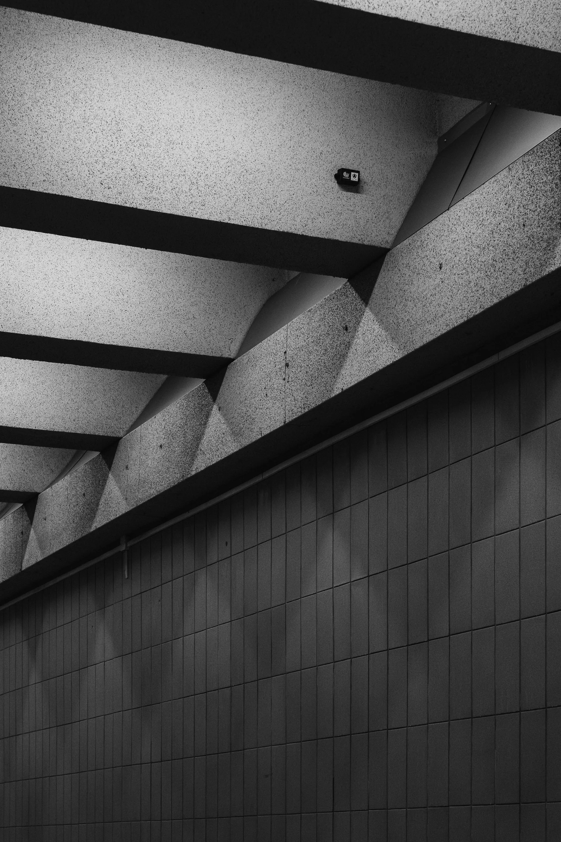 Diagonal concrete beams and a tiled wall form a graphic black-and-white underpass ceiling.