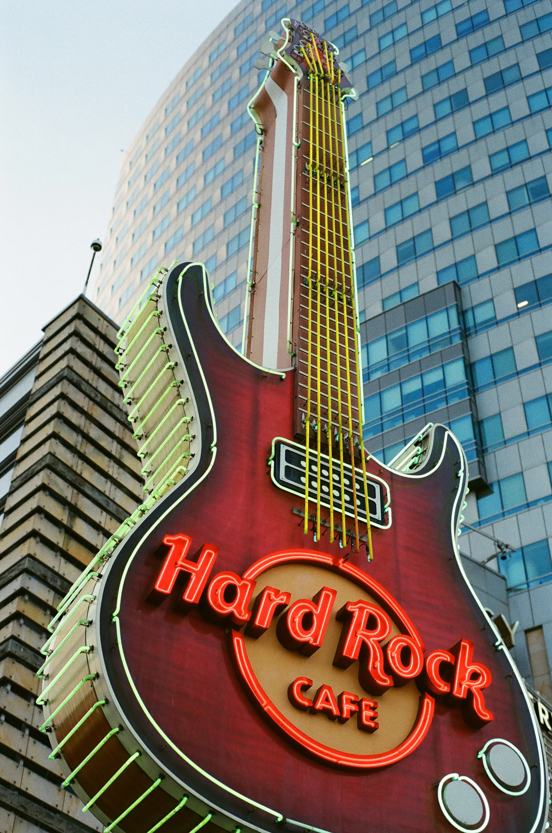 A giant Hard Rock Cafe guitar sign stands against a glass office tower in Warsaw.