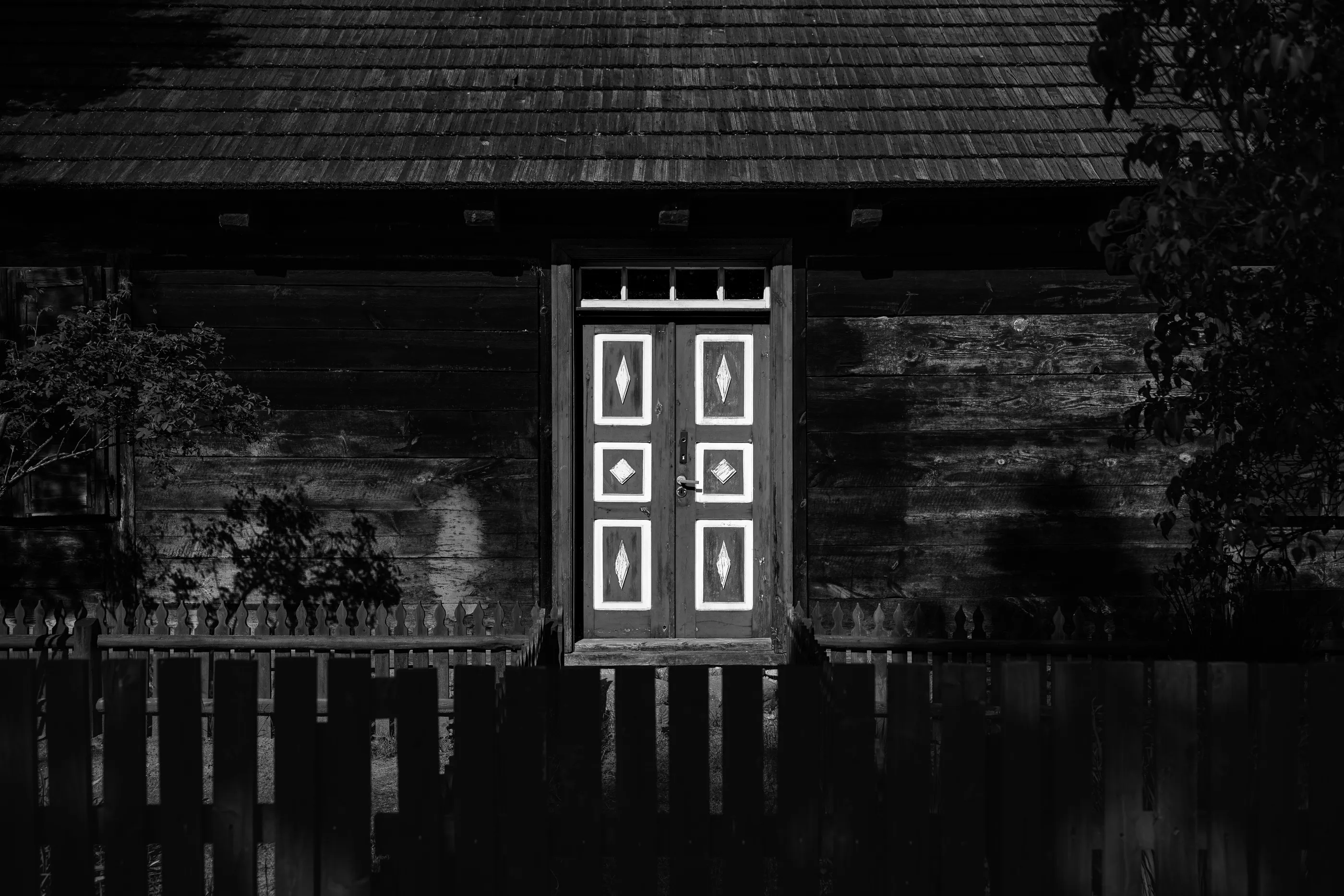 A traditional wooden cottage door with diamond-carved panels, photographed in black-and-white.